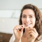 Woman looking at camera, smiling, holding Invisalign clear aligner