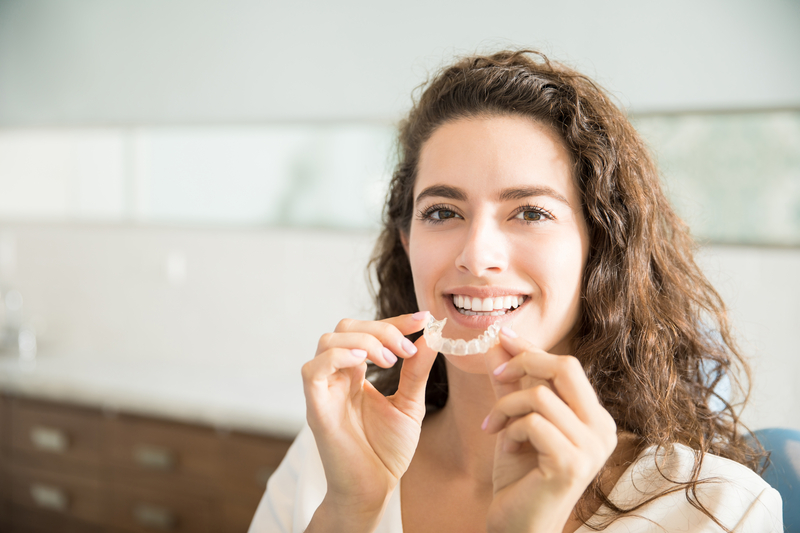 Woman looking at camera, smiling, holding Invisalign clear aligner