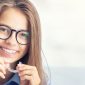Teen girl with glasses smiling at camera holding Invisalign clear aligners